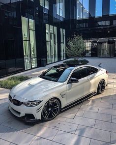 a white car parked in front of a tall building with glass windows and black rims