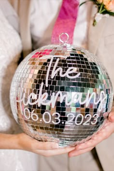 a bride and groom holding up a disco ball ornament for their wedding day