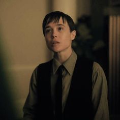 a young man wearing a vest and tie looking at the camera in a dimly lit room