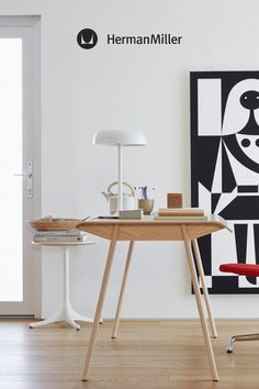 a desk with a red chair in front of it and a black and white painting on the wall