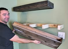 a man is holding some wood in front of two wooden shelfs on the wall