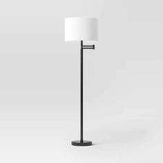 a black floor lamp with a white shade on the top and bottom part of it