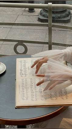 a woman sitting at a table reading a book with her hands on top of it