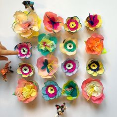 several colorful paper flowers are arranged on a white surface, with one person pointing at them