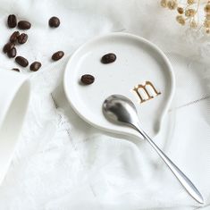 a spoon and some coffee beans on a plate with the letter m spelled in it