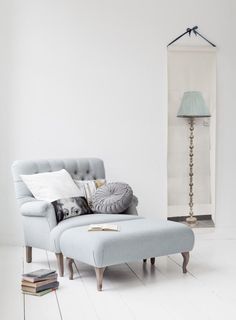 a chair and ottoman in a white room with a lamp on the wall behind it