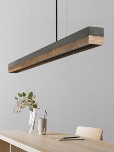 a wooden table topped with a vase filled with flowers and greenery next to a light fixture