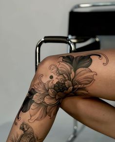 a woman sitting on a chair with her legs crossed and flowers tattooed on the leg