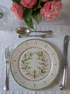 there is a place setting with pink flowers in the vase and silverware on the table