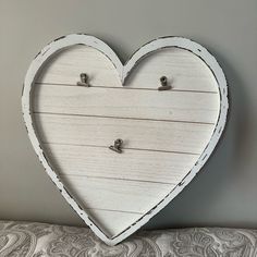 a white heart shaped wooden frame with two hooks attached to it on a wall above a bed