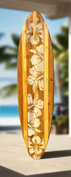 a wooden surfboard with white flowers and leaves on it's side, in front of a beach