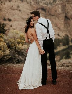 a bride and groom standing together in the desert looking at each other while holding hands