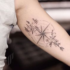 a woman's arm with a compass and flowers tattoo on the left inner arm