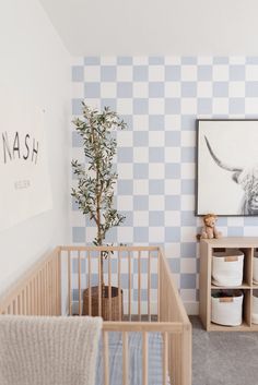 a baby's room with blue and white checkered wallpaper, a crib, and a small tree in the corner