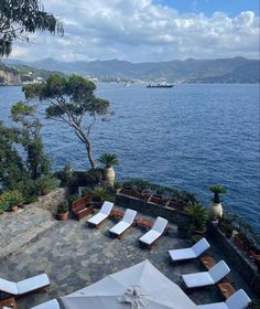 an outdoor seating area with umbrellas and chairs overlooking the water in front of some mountains