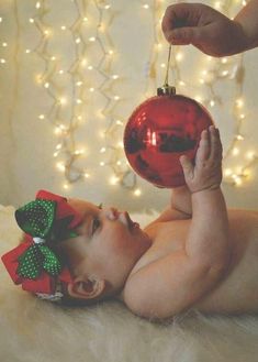 a baby laying on its back with a christmas ornament hanging from it's head