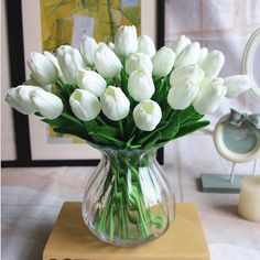 a vase filled with white tulips sitting on top of a wooden table next to a mirror