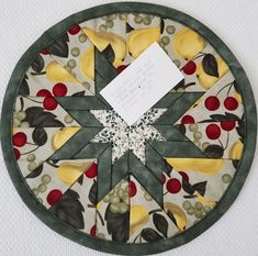 a piece of paper is placed on top of a quilted circular design with fruit and leaves