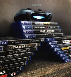 a stack of video games sitting on top of a wooden table next to a game controller