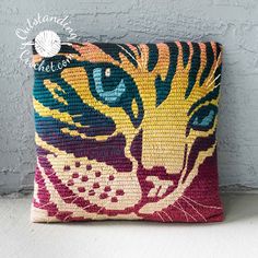 a colorful pillow with a cat's face on it, sitting against a wall