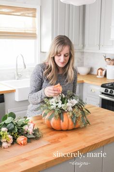 a woman is decorating a pumpkin in the kitchen with greenery and flowers on the counter