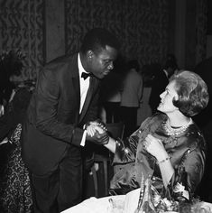 a man in a tuxedo is shaking hands with a woman at a dinner table