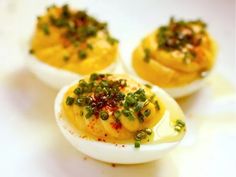 three deviled eggs topped with green onions and chives on a white plate, ready to be eaten