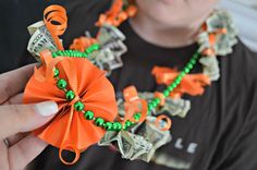 a person is holding a necklace made out of dollar bills and orange ribbon with green beads