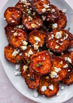 a white plate topped with fried potatoes covered in feta cheese and garnished with herbs