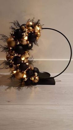 a black and gold christmas wreath with lights on the top is sitting in front of a white wall