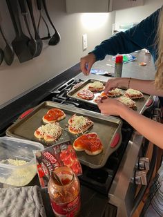 two girls making mini pizzas on top of an oven with cheese and tomato sauce