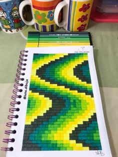 a spiral notebook with legos on it next to two coffee mugs