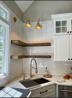 a kitchen with white cabinets and open shelving above the sink in front of a window