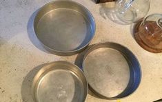 three metal pans sitting on top of a counter next to a glass jar and knife