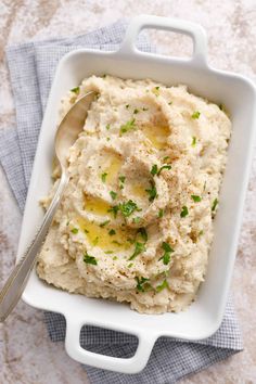 mashed potatoes in a white dish with a spoon on the side and garnished with parsley