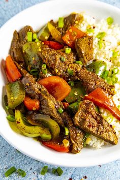 a white plate topped with meat and veggies next to rice on top of a blue table