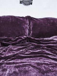 a bed covered in purple sheets and pillows with a pillow on top of the comforter