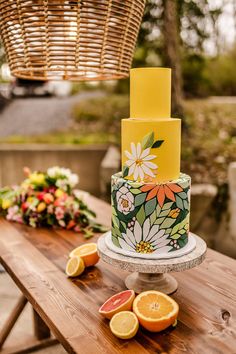 a colorful cake sitting on top of a wooden table next to flowers and oranges