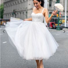 a woman in a white dress is walking down the street and holding a flower bouquet