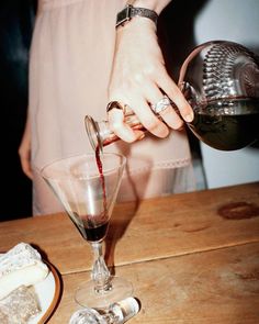 a person pouring wine into a glass on top of a wooden table next to other items