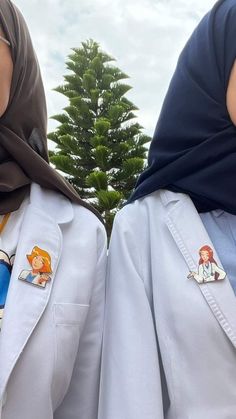 two women wearing white coats with cartoon stickers on their jackets and headscarves