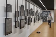 a man walking down a hallway next to a wall covered in pictures and framed photographs