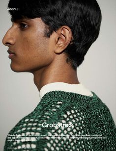 a young man with black hair wearing a green and white sweater looking off to the side