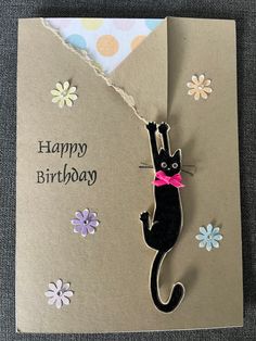 a birthday card with a black cat hanging from it's side on a table