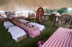 several picnic tables covered in red and white checkered cloths under a tent with hay bales