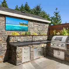 an outdoor kitchen with grill and television on the wall