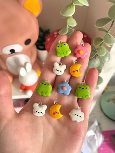 a hand holding some tiny charms in front of a teddy bear and flower potted plant