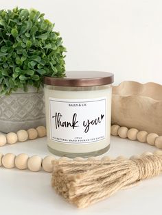 a thank you candle surrounded by wooden beads and a potted plant on a table