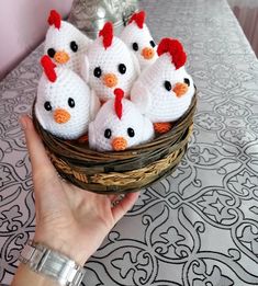 a person holding a basket filled with small crocheted chicken toys on top of a table