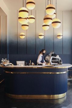 a woman sitting at a counter in front of a blue and gold bar with lights hanging from the ceiling